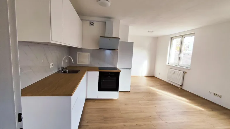 Moderne Einbauküche mit weißen Schränken, Holz-Arbeitsplatte und offener Gestaltung zum Wohnbereich.