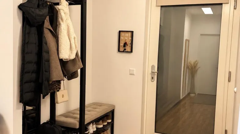 Heller Eingangsbereich mit Garderobe, Schuhbank und Holzboden, der zu weiteren Räumen führt.