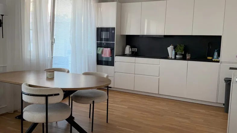Moderne Küche mit weißen Hochglanzfronten, schwarzer Arbeitsplatte und integriertem Essbereich.