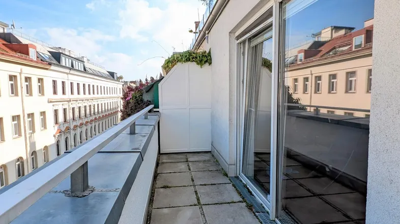 Schmaler Balkon mit Fliesenboden und Blick auf die umliegenden Stadtgebäude unter blauem Himmel.