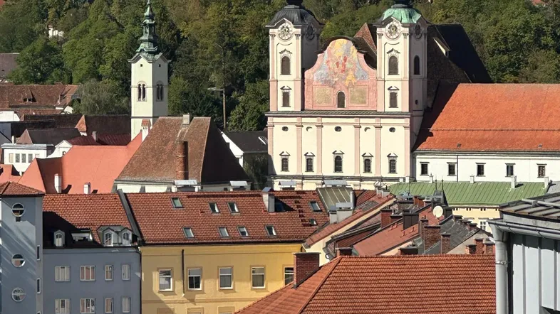 Panoramablick über eine historische Stadt mit markanten Kirchtürmen und grünen Hügeln im Hintergrund.