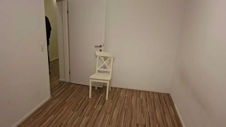 Leeres Zimmer mit Laminatboden und weißer Tür, bereit zur individuellen Gestaltung.