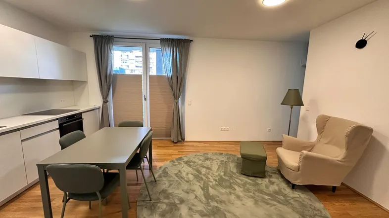 Heller offener Wohn- und Essbereich mit moderner Küche, Holzboden und Zugang zum Balkon.