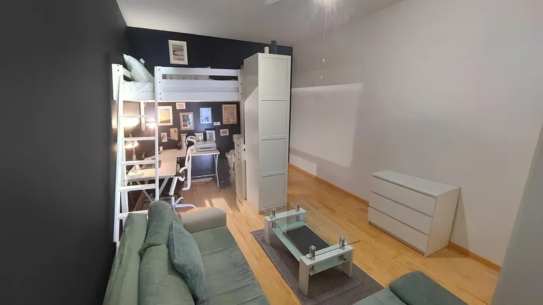 Helles Wohnzimmer mit Hochbett, Sofa und Arbeitsbereich, ideal für ein Studio-Apartment.