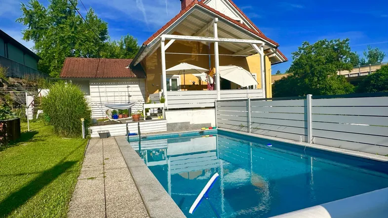 Außenansicht des Hauses mit großem Swimmingpool und gepflegtem Garten unter blauem Himmel.