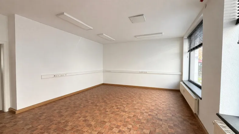 Leerer Büroraum mit Parkettboden, weißen Wänden und großen Fenstern für viel Tageslicht.