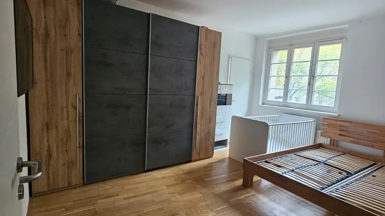 Geräumiges Schlafzimmer mit Holzbettrahmen, Babybett und großem Schiebetürenschrank, hell und funktional.