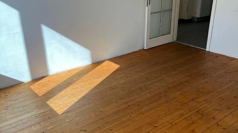 Helles Zimmer mit Holzdielenboden und viel natürlichem Licht durch die Tür.