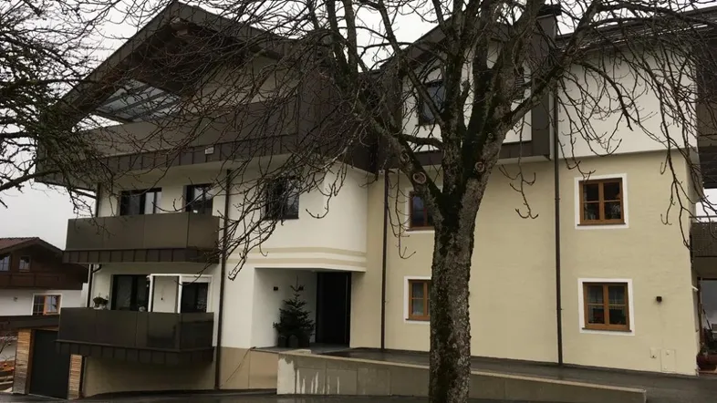 Mehrstöckiges Wohngebäude mit heller Fassade, dunklem Dach und einer Rampe am Eingang.