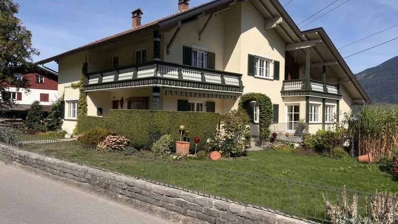 Traditionelles Wohnhaus mit gepflegtem Vorgarten, Balkonen und Blick auf die umliegende Landschaft.