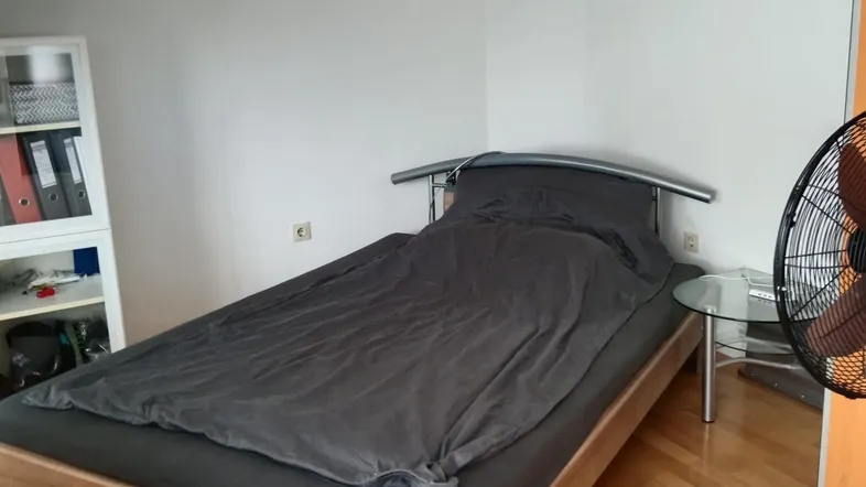 Helles Schlafzimmer mit Holzbett, Parkettboden und Dachschräge, funktional und ordentlich eingerichtet.