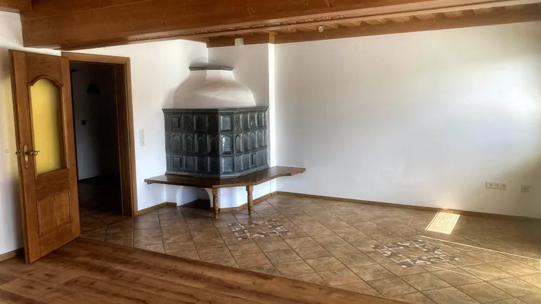Geräumiges Wohnzimmer mit traditionellem Kachelofen, Holzbalkendecke und einer Kombination aus Fliesen- und Laminatboden.