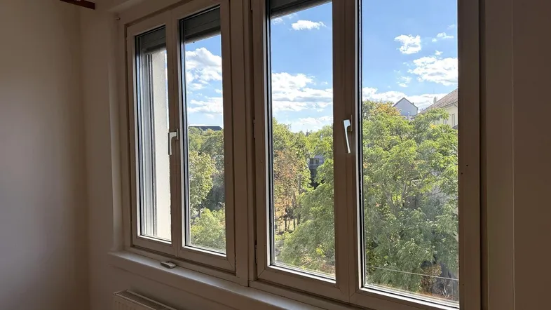 Fenster mit Blick ins Grüne und blauen Himmel, das viel Tageslicht in den Raum lässt.