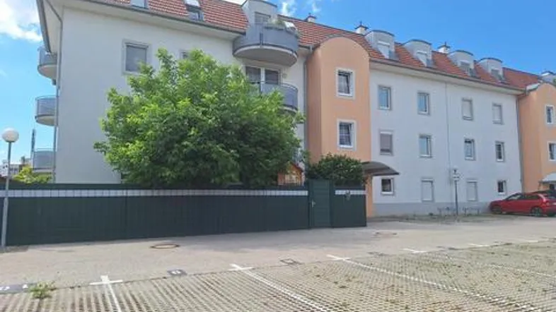 Mehrfamilienhaus mit Balkonen und Außenparkplätzen unter blauem Himmel.