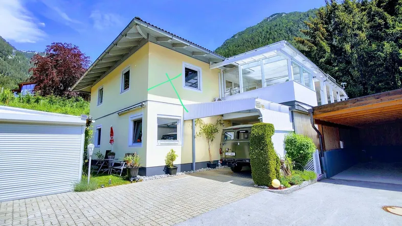 Hausfassade mit Wintergarten, Carport und Blick auf die umliegenden Berge.