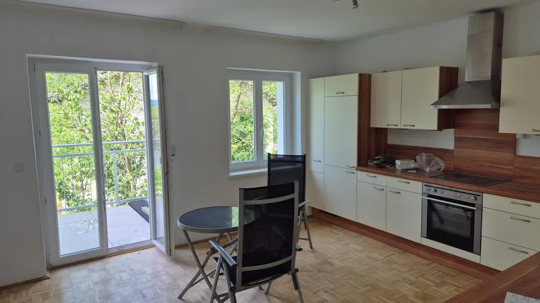 Helle Küche mit Einbauschränken, Kochfeld und Zugang zu einem Balkon mit grüner Aussicht.