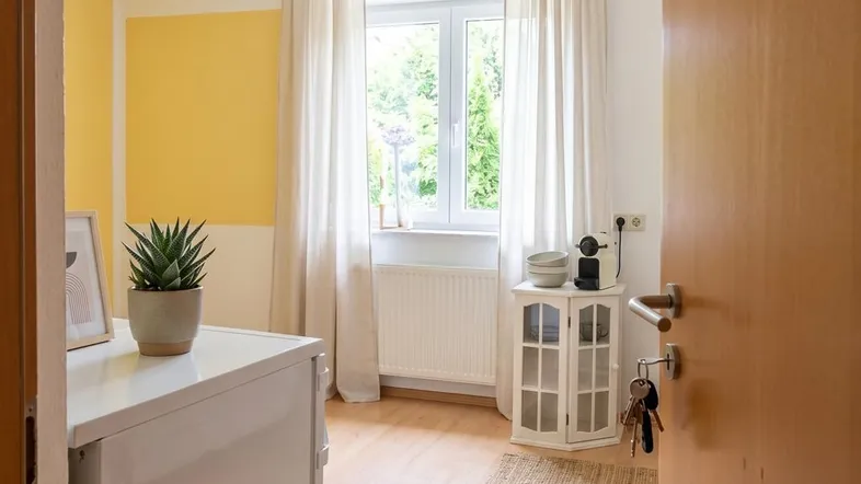 Heller Eingangsbereich mit gelber Akzentwand, Fenster und Blick ins Grüne.