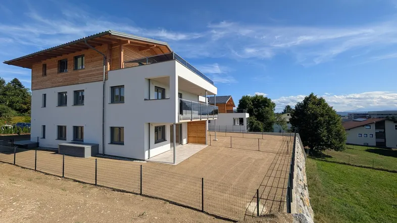 Neubau-Mehrfamilienhaus mit moderner Architektur, Balkonen und Terrassen in ländlicher Umgebung.
