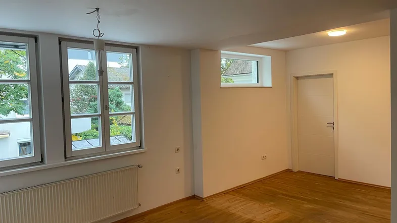 Helles Zimmer mit Holzparkettboden, großen Fenstern und Heizkörpern, bereit zur individuellen Gestaltung.