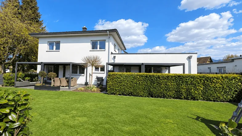 Großzügiger Gartenbereich mit gepflegtem Rasen, Hecke und moderner Terrasse am Haus.