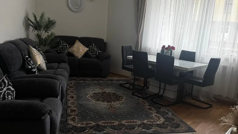 Geräumiger Wohn-Essbereich mit dunklem Sofa, Esstisch und Parkettboden, hell durch große Fenster.