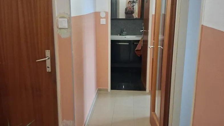 Langer Flur mit Fliesenboden und Türen zu verschiedenen Räumen, inklusive Blick ins Badezimmer.