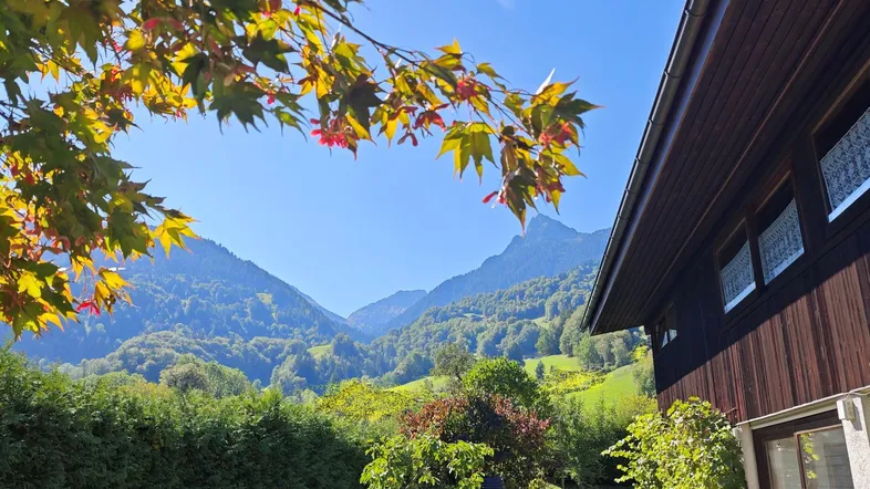 Hausfassade mit Holzelementen und einem atemberaubenden Blick auf die umliegende Berglandschaft an einem sonnigen Tag.