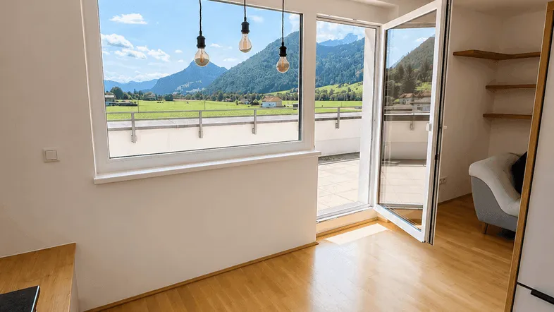 Heller Wohnbereich mit Holzboden, Bergblick und Zugang zu einer großen Terrasse.