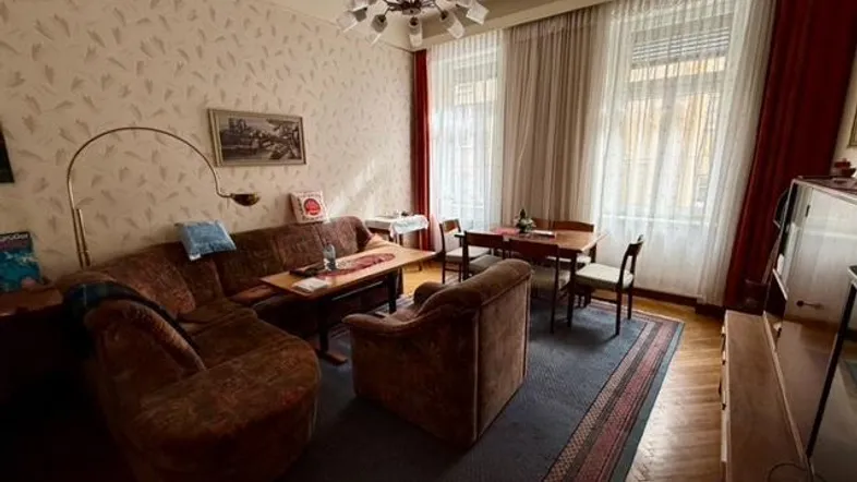 Gemütliches Wohn-Esszimmer mit traditioneller Einrichtung, Tapetenmuster und Blick auf die Fenster.