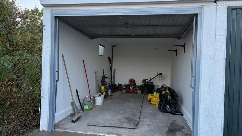Offene Garage mit Betonboden, genutzt als Abstellraum für Gartengeräte und Werkzeuge.
