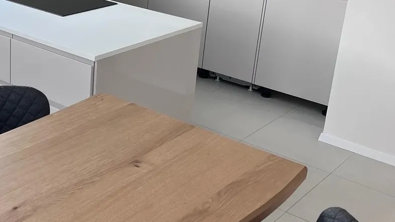 Moderne Küche mit hellgrauen Schränken, weißer Arbeitsplatte und integriertem Essbereich.