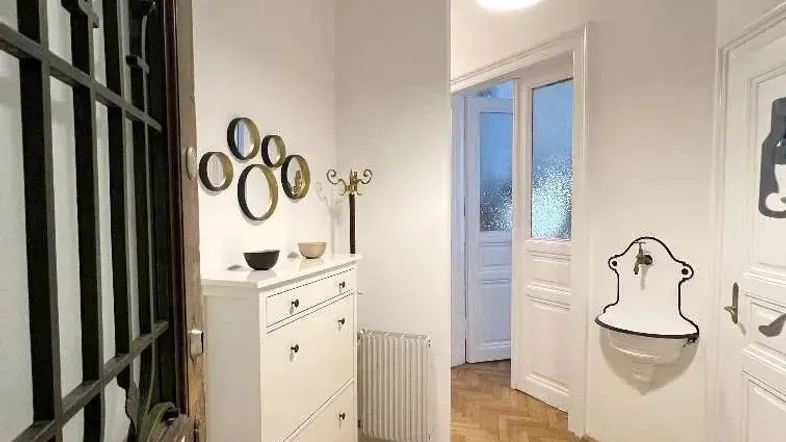 Heller Eingangsbereich mit Fischgrätparkett, weißer Schuhkommode und dekorativen Spiegeln an der Wand.