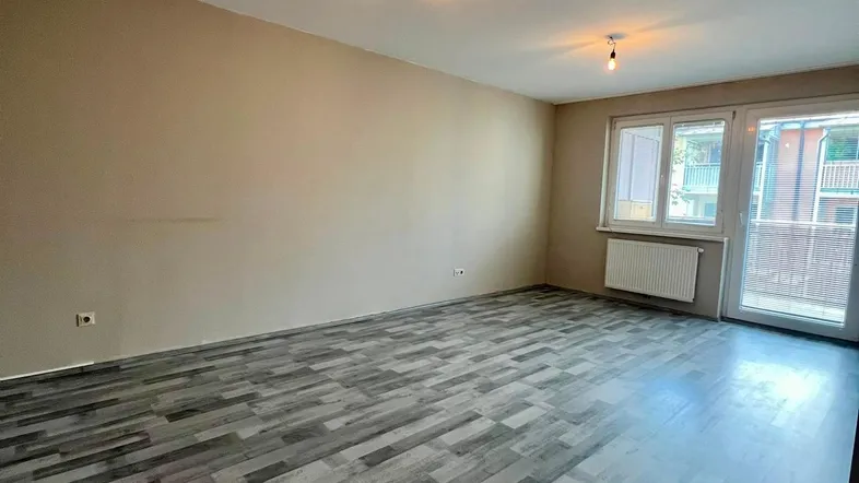 Geräumiges Wohnzimmer mit modernem Laminatboden und Zugang zum Balkon, hell und unmöbliert.