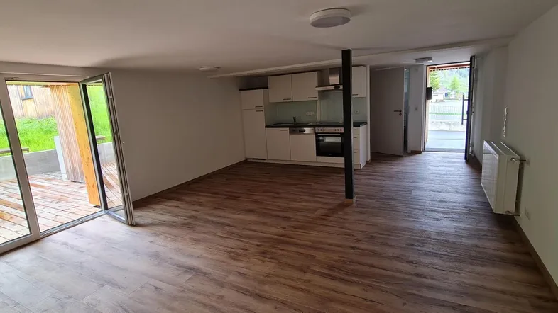 Heller offener Wohnbereich mit Holzboden, integrierter Küchenzeile und Zugang zu einer Holzterrasse.