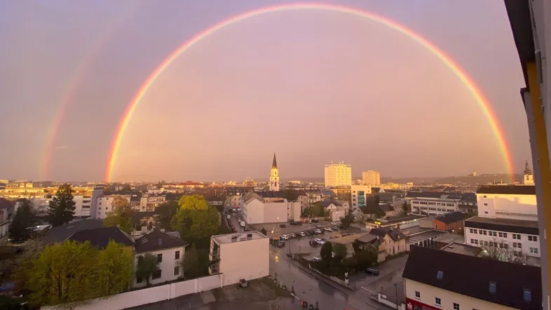 Panoramablick über die Stadt mit einem doppelten Regenbogen am Abendhimmel, aufgenommen von einem oberen Stockwerk.