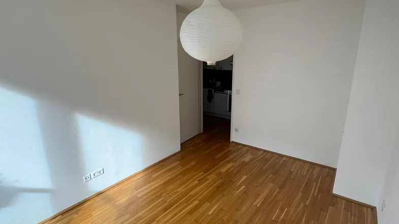 Helles, leeres Zimmer mit Parkettboden und Zugang zu einem weiteren Raum, ideal als Wohnbereich.