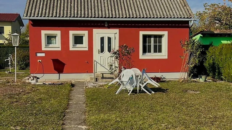 Rotes Einfamilienhaus mit weißem Dach und grünem Garten unter blauem Himmel.