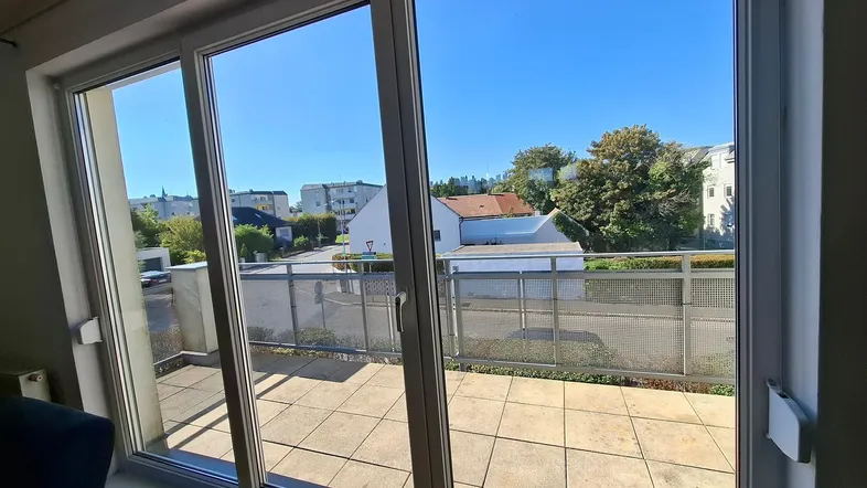 Helle Aussicht aus einem Innenraum auf eine große geflieste Terrasse mit Blick auf die Umgebung.