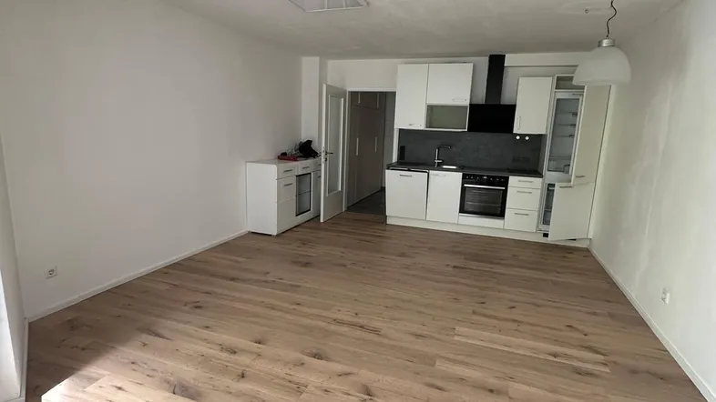 Heller offener Wohnbereich mit integrierter Küche, modernem Holzboden und weißen Wänden.