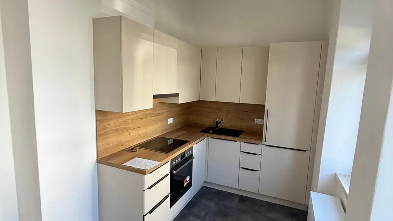 Moderne Einbauküche mit hellen Schränken, Holzoptik-Arbeitsplatte und dunklem Fliesenboden.