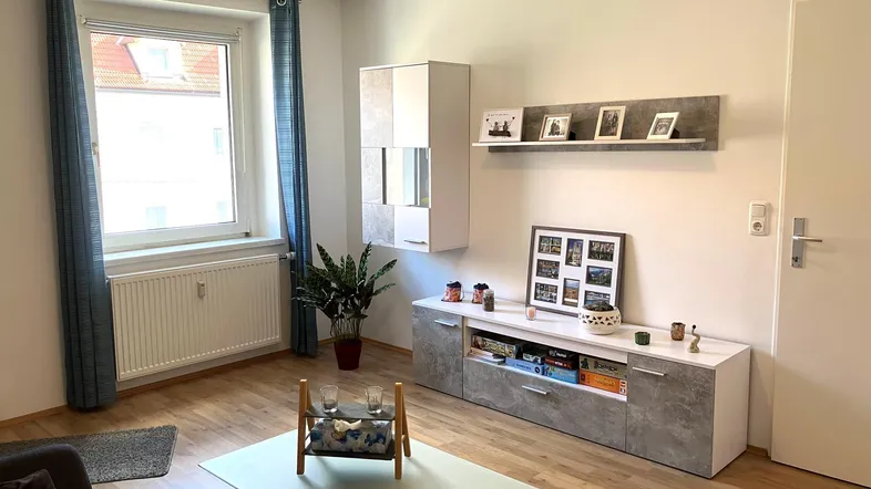 Helles Wohnzimmer mit modernem Medienmöbel, Parkettboden und Fenster mit blauen Vorhängen.