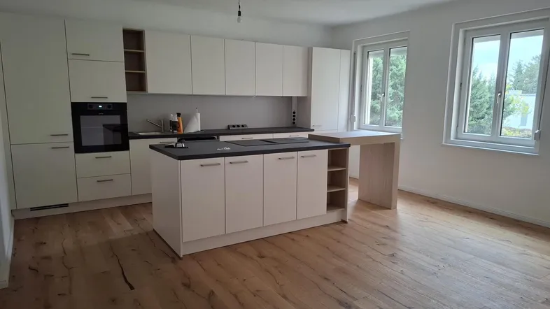 Moderne, helle Küche mit weißer Einbauküche, Kochinsel und Holzboden, bietet viel Tageslicht durch große Fenster.
