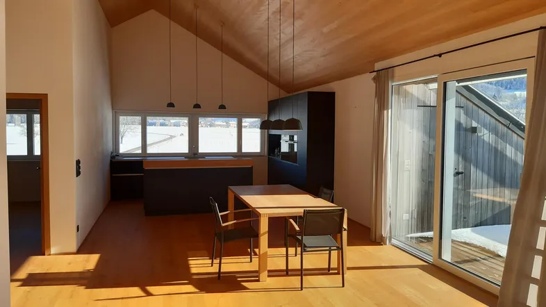 Heller offener Wohn-Essbereich mit moderner Küche, Holzboden und Zugang zum Balkon mit Bergblick.