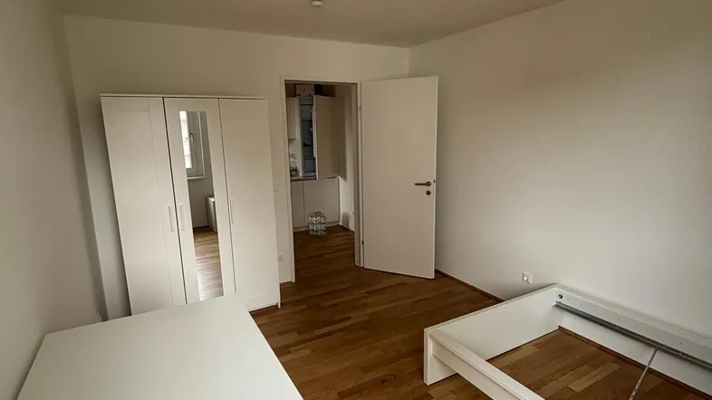 Helles Schlafzimmer mit Parkettboden, weißem Kleiderschrank und Bettrahmen, bereit zur individuellen Einrichtung.