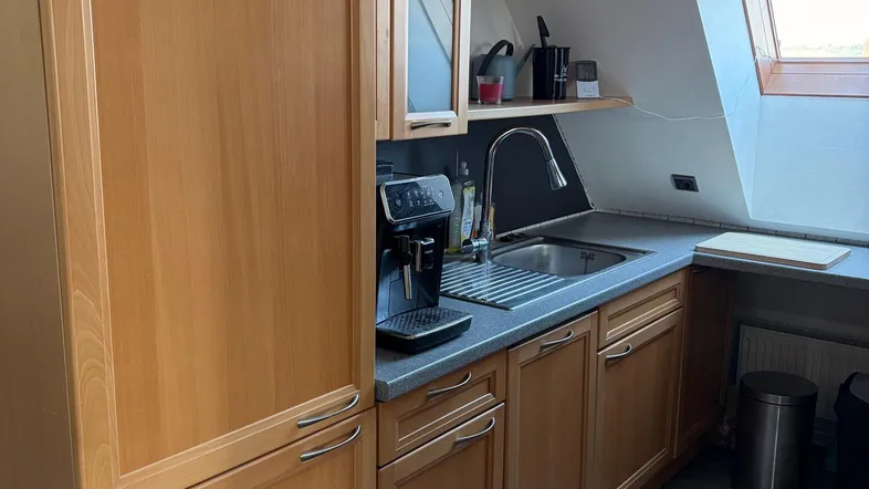 Helle Küche im Dachgeschoss mit Holzschränken, Spüle, Kaffeemaschine und einem Dachfenster für viel Tageslicht.