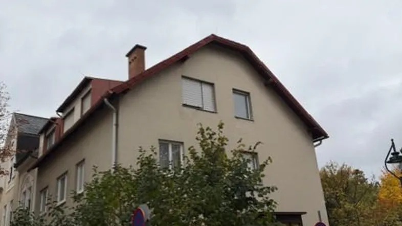 Klassisches Wohnhaus mit Satteldach und beiger Fassade, umgeben von Bäumen und Grünflächen.
