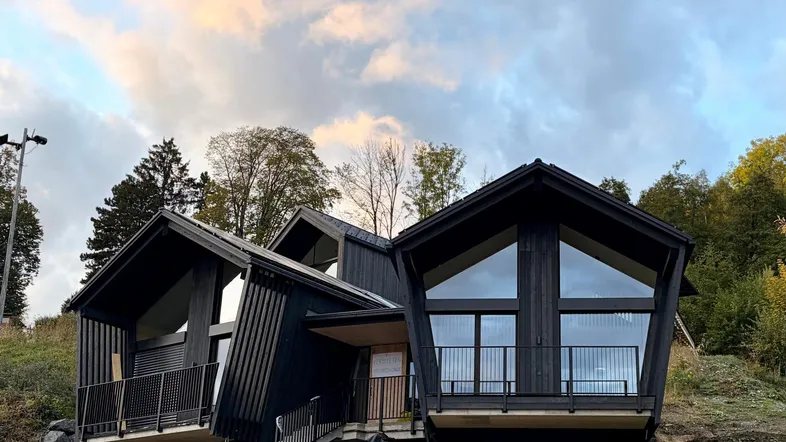 Modernes, dunkles Holzhaus mit markanter Architektur und großen Fenstern in alpiner Umgebung.