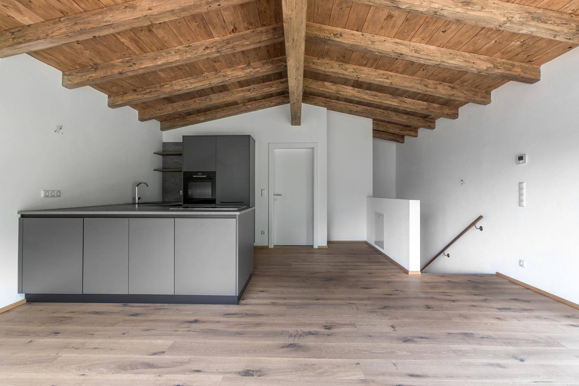 Moderne Küche in Grau mit Holzbalkendecke und Eichenparkett in einem offenen Wohnbereich.