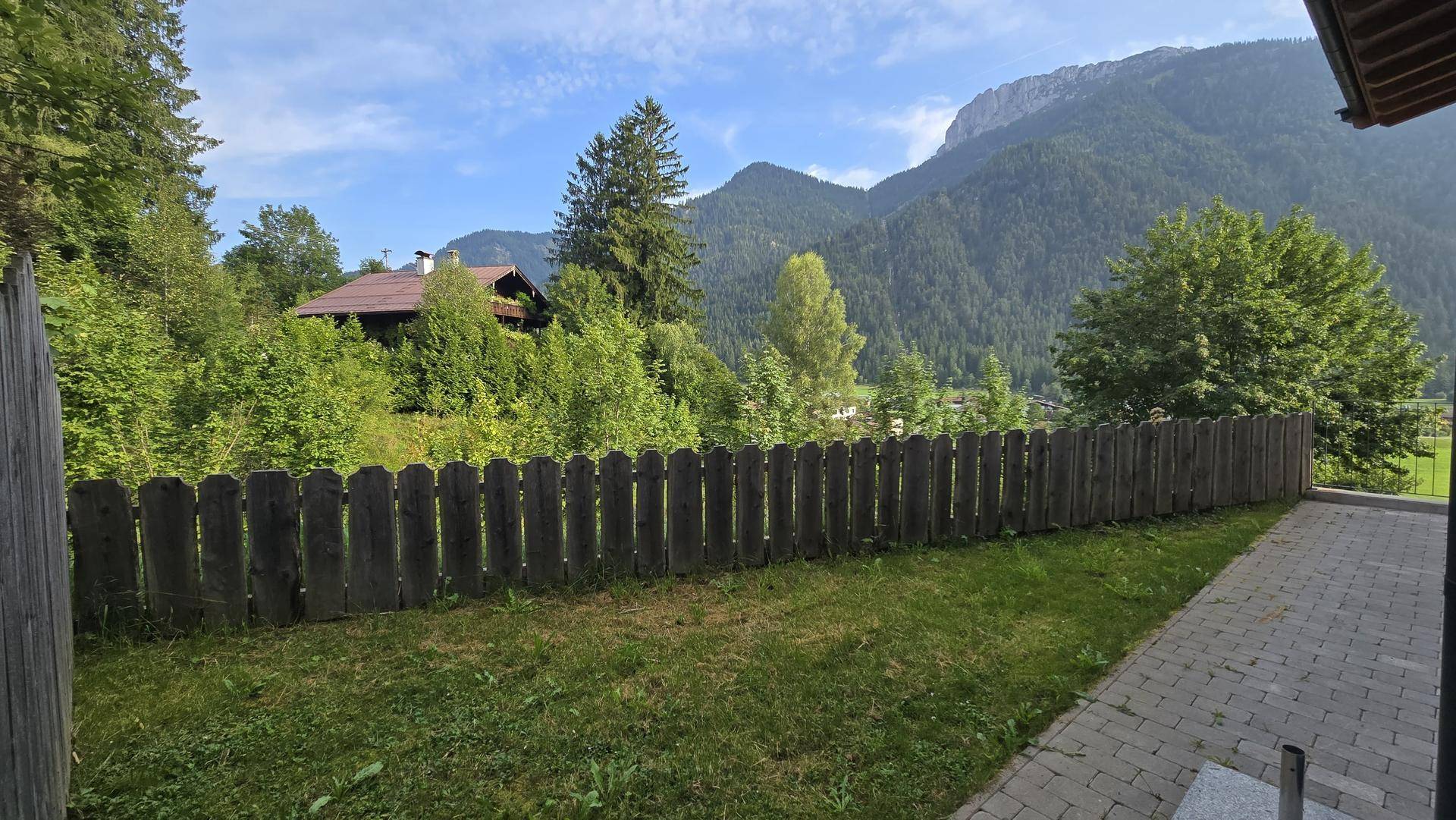 Kleiner Gartenbereich mit Rasenfläche, Holzzaun und Blick auf die umliegenden Berge.