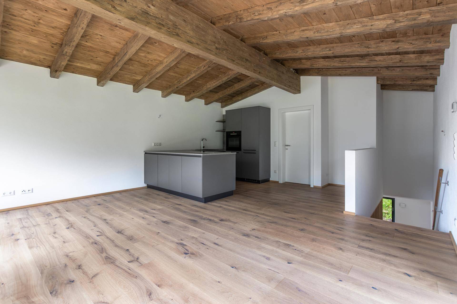 Helle, offene Küche mit moderner Kücheninsel, Holzbalkendecke und hochwertigem Holzfußboden.